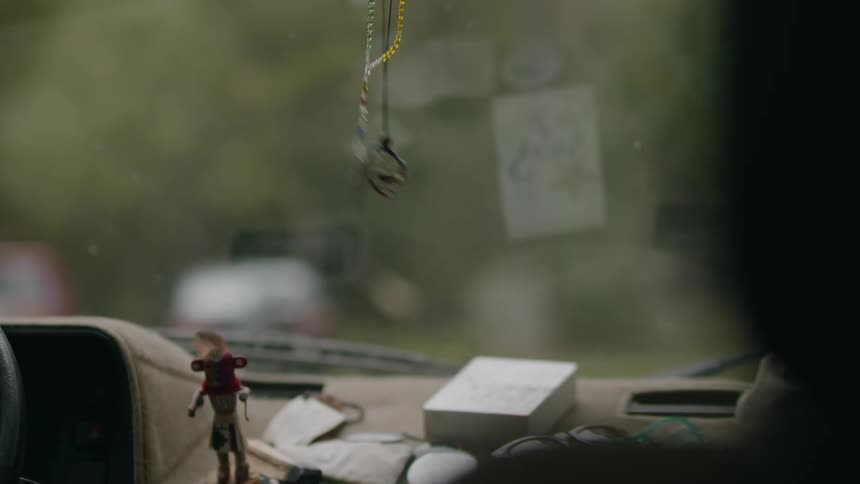 Crucifix on beaded string sways as it hangs from rearview mirror