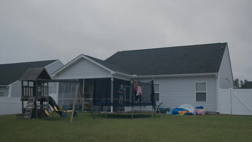 Happy kids jumping on a trampoline set on the backyard of a house at evening