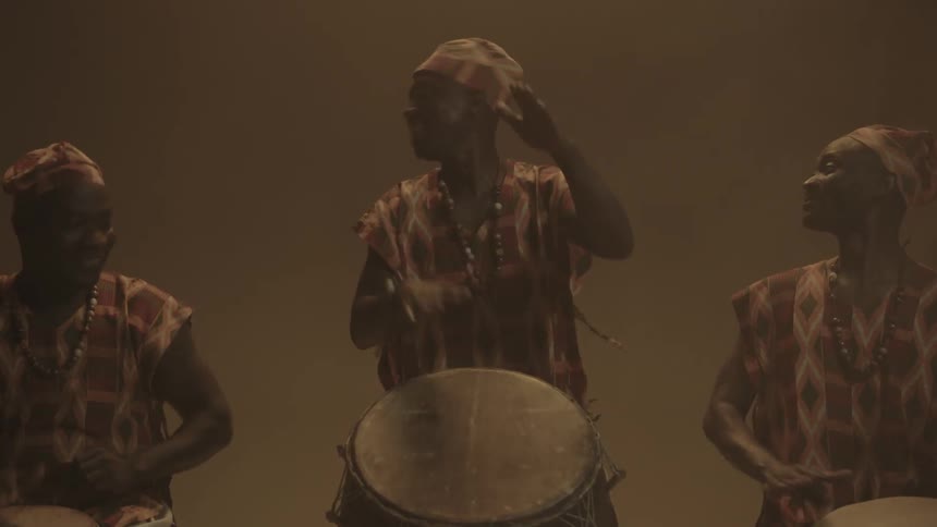 Three people perform dancing and playing drums