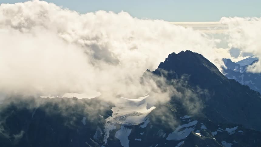 Dense clouds move over the peaks of snow capped mountains