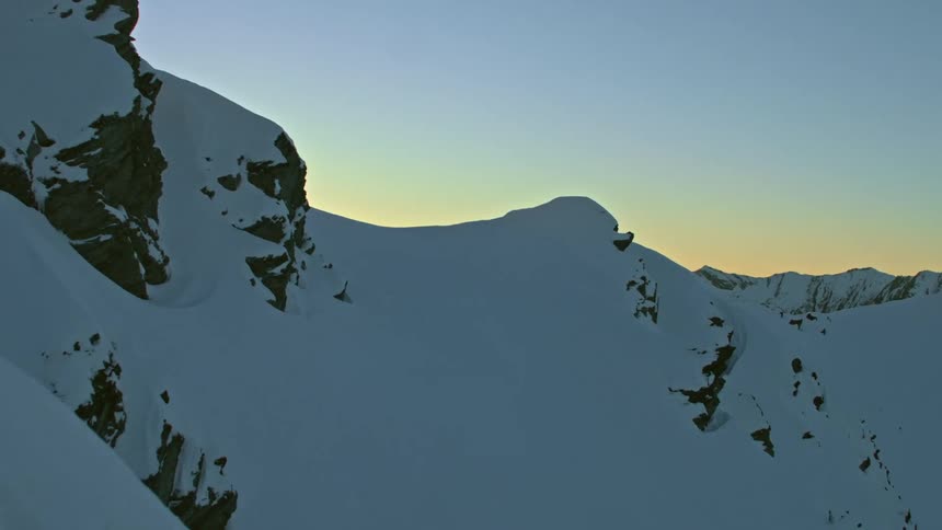 Ridgeline reveal of the sun glowing in the sky behind snow covered mountains