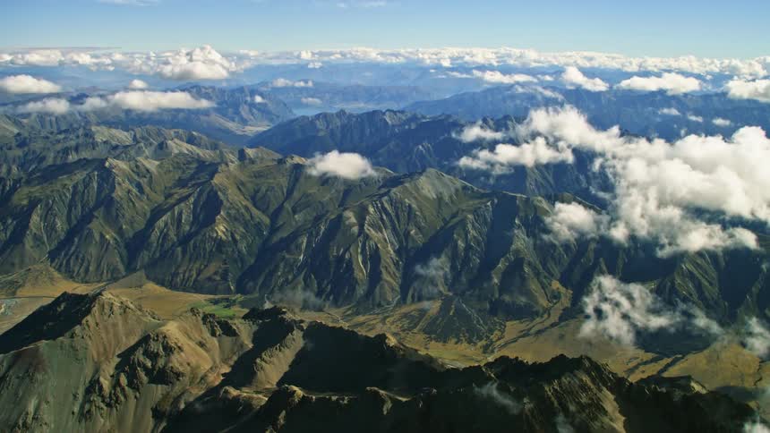 Aerial view of white clouds floating over the peaks and slopes of a mountain range
