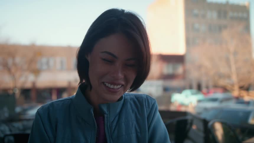 A woman looks up and smiles and laughs near a business parking lot in a small town