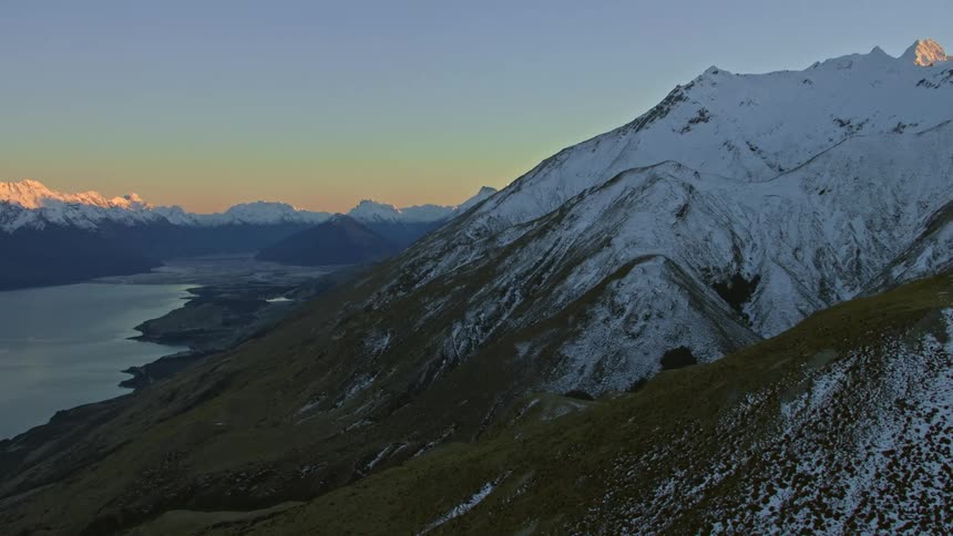 An aerial view of a snowy mountain range and body of water at sunrise