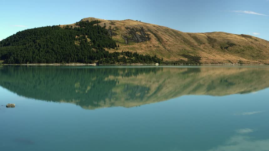 A cliff reflects off clear blue lake water aerial