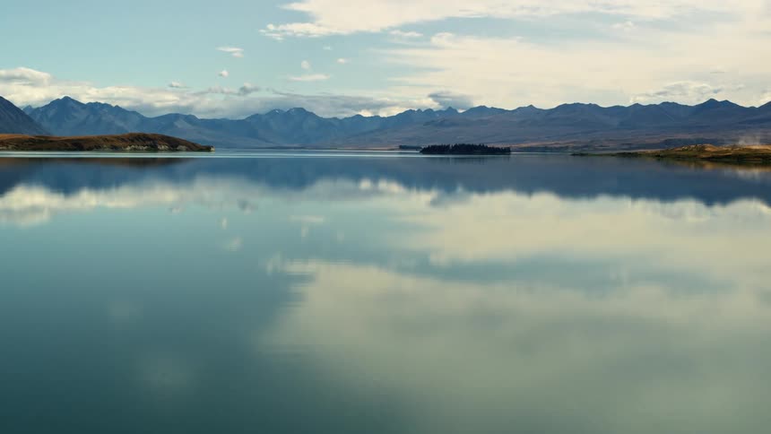 Aerial view of the calm surface of a lake next to a mountain range at morning