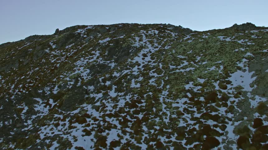 Helicopter reveals snow dusted slope and ridge leads to a mountain valley and view