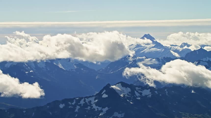Aerial view of white clouds floating over the slopes covered in snow of a mountain range