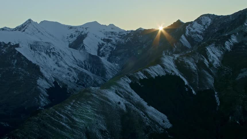 The sun shines over a snow covered mountain under a clear sky