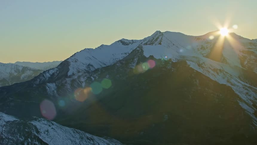 Aerial view of sunlight over the snow covered peaks of a mountain range at morning