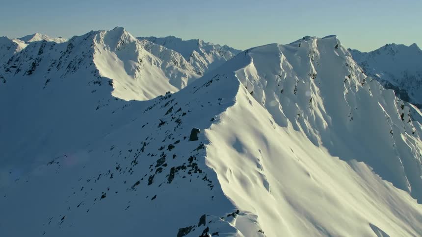 The sun shines on snow covered mountains with peaks high in a clear sky