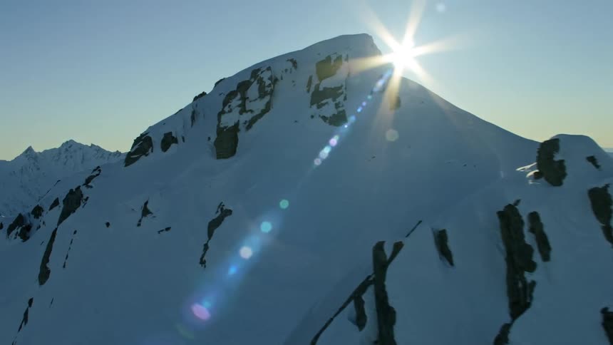 Aerial view of snowy mountain range and sun flare shining brightly