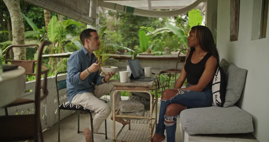A man is eating as he talks with a woman