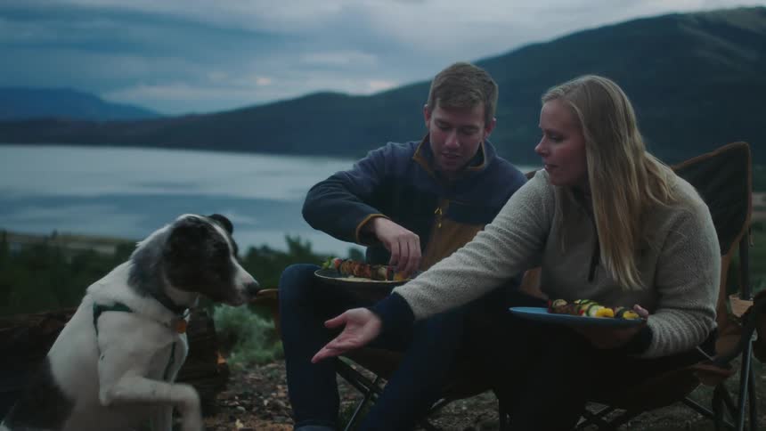 A man and woman eat and shake their dogs hand