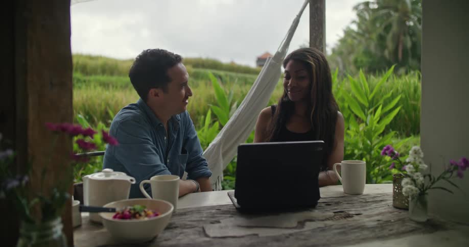 Young couple sitting on a table in the patio looking at a laptop next to a field