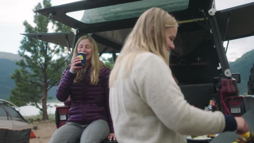 A woman sips her coffee as she laughs with a friend at the grill