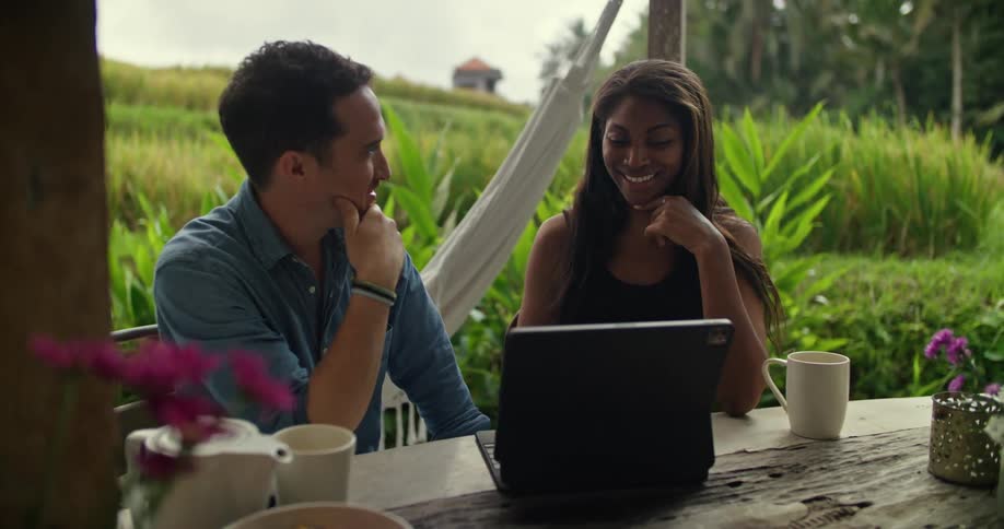 A man and woman outdoors using a laptop