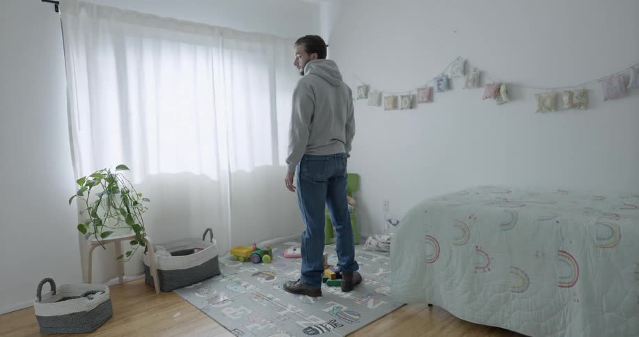 A man is standing in a kids room and turns his head to look