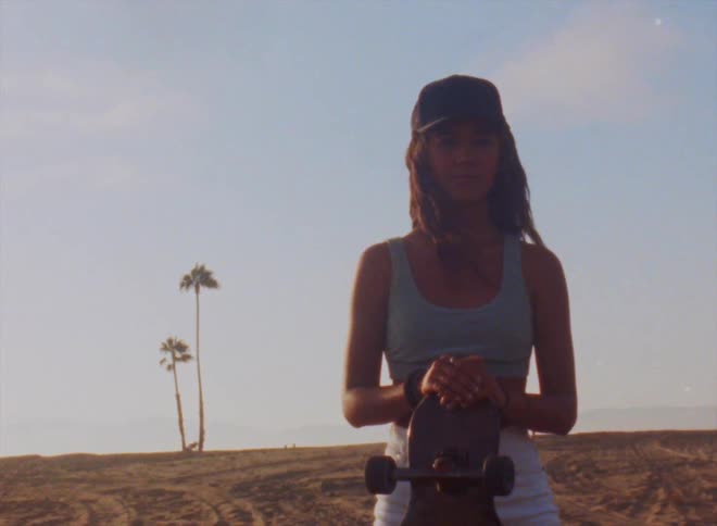 A woman poses on the beach holding her skateboard