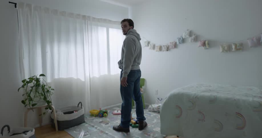 A spotlight shines in the dark bedroom where a man stands