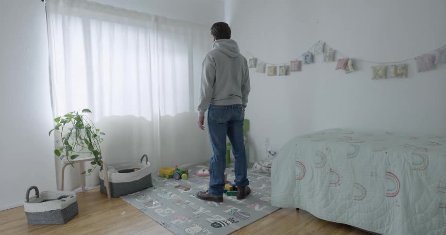 Man standing in a girls room at night looks at white lights pass by the window