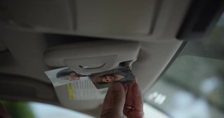 A person hangs small photographs on the sunscreen of a moving car at daytime