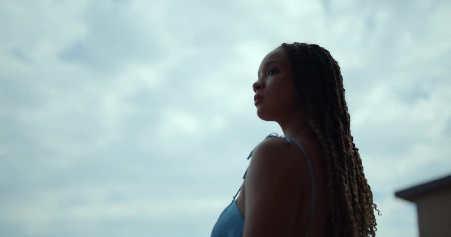 A woman looks around her as she stands outside on a cloudy day