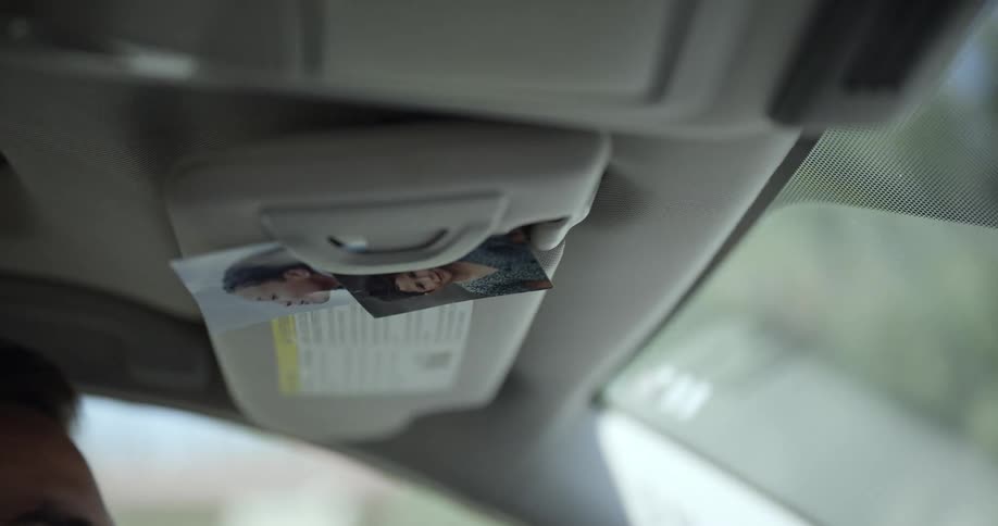 Close up of photos hanging from the sunshade on a moving car at daytime