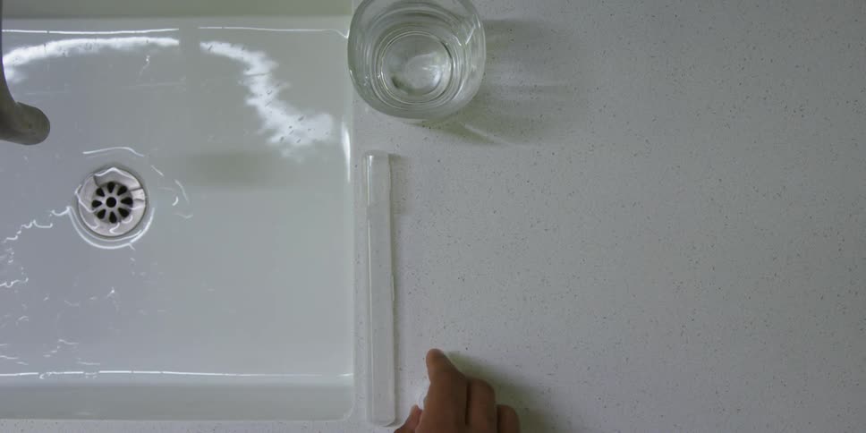 A person is at a sink with a glass and puts toothpaste on a toothbrush