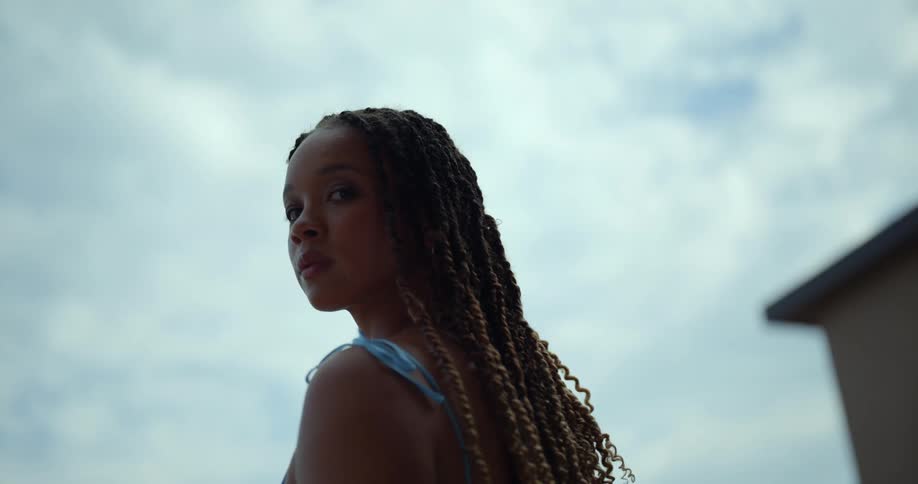 A woman walking outdoors during the day looks over her shoulder into the camera