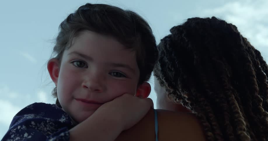 A little girl is in her mothers arms with a smile on her face as she rests on her shoulder