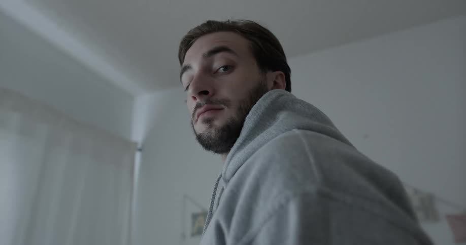 Man standing in a girls room at night looks at the camera while white lights pass by the window