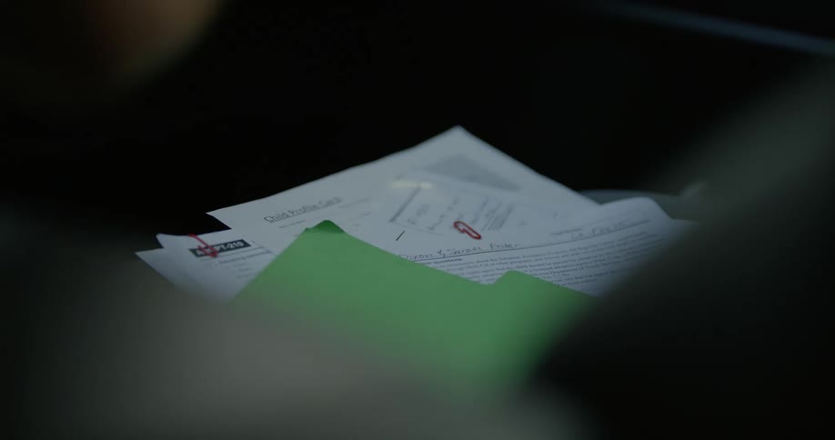 Person picks up small picture of a child from among papers in file folder lying on car seat