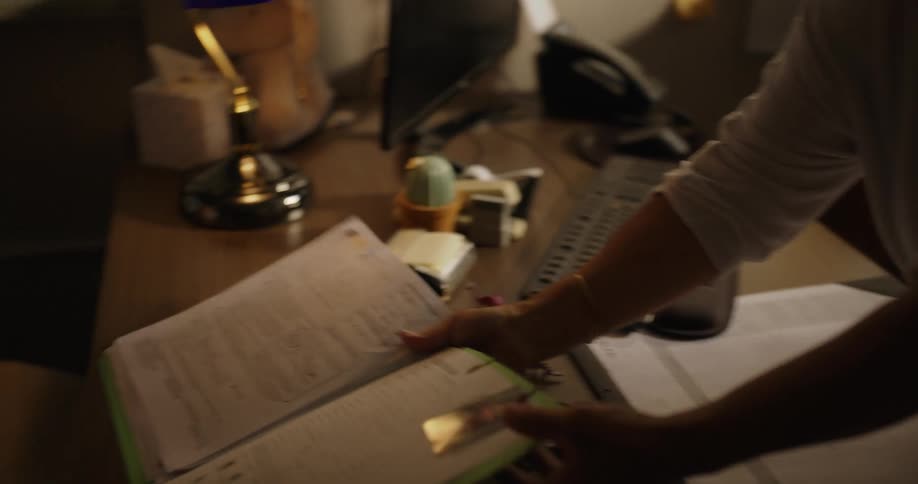 A man and woman are sitting down in an office as a woman opens a file with a photograph and fingerprints and sets it on the desk in front of them