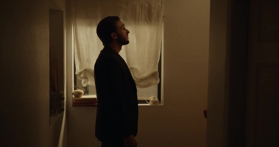 Man following a woman inside a house stops for a moment at the stairs next to a window