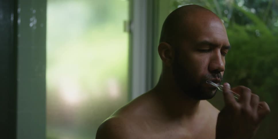 A bald man brushing his teeth with his eyes closed