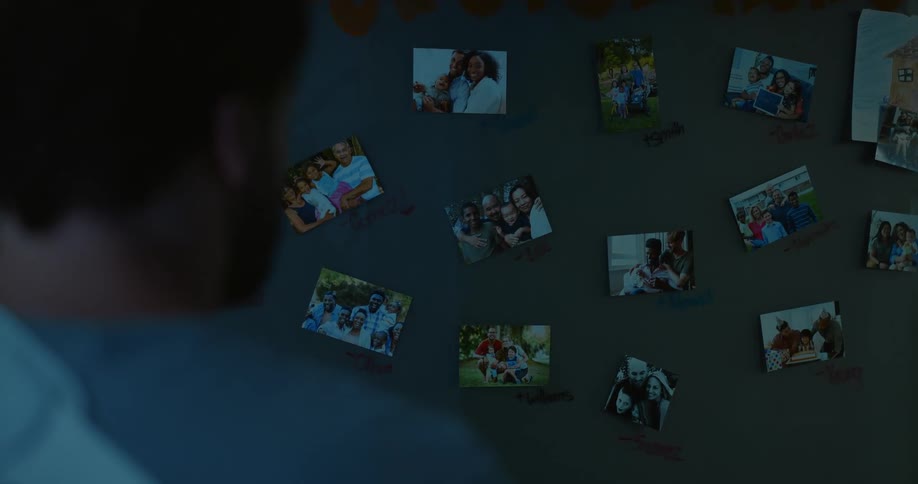 Injured man stands in a dimly lit room looking at photos hanging from the wall
