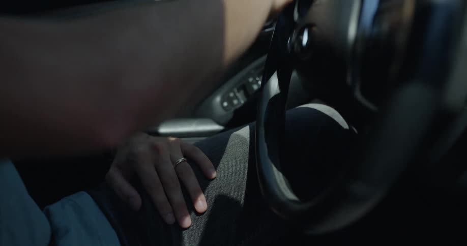 Man with gray pants blue t shirt and black wristwatch plays with ring while driving car