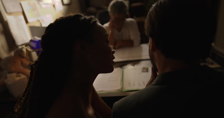 A couple smiles and kisses as they sit at a desk in an office with a worker