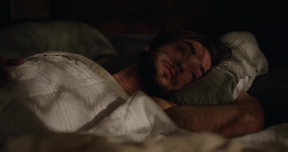 Muscular man with beard wakes up in bed in the morning