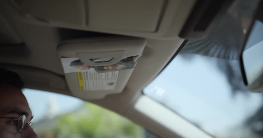 A man wearing glasses is driving his car through a neighborhood
