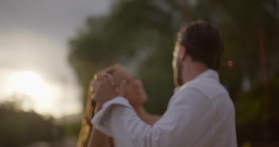 Man with beard and white shirt dances with woman with dreadlocks and white dress next to road at sunset in the countryside