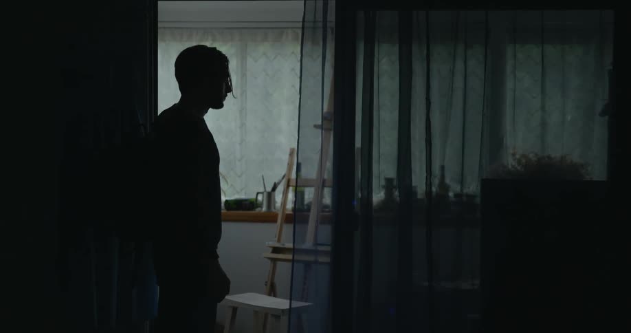 Boy looking down is silhouetted against the window in room