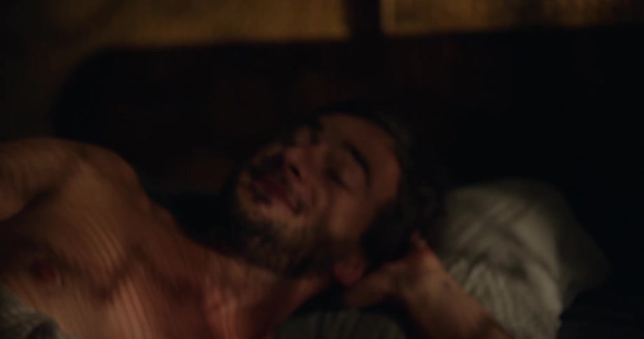 Shirtless man with beard wakes up lying in bed in the morning