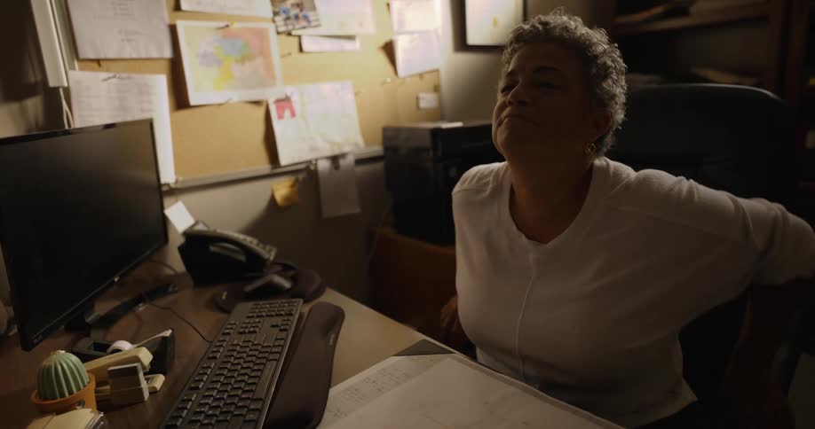 Woman sitting on a chair in front of a desk in the office nods while listening to someone