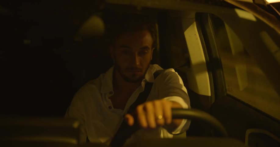 Man steers car along highway as front windshield reflects light of streetlights