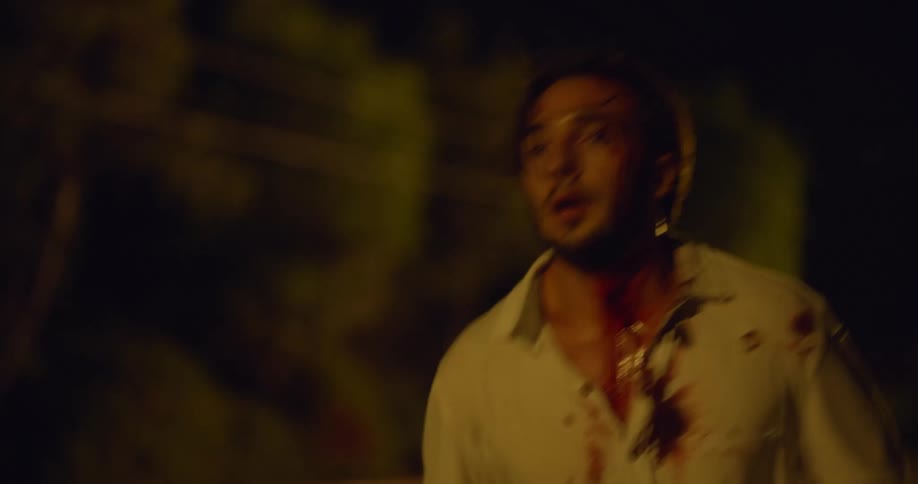 A man is running down the dark road covered in blood