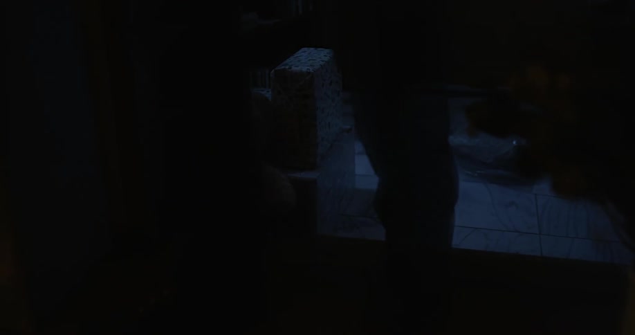 Man walks past a teddy bear on the floor of a room at night