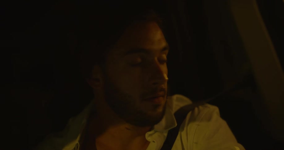 Man with beard and white shirt looks around while driving car at night