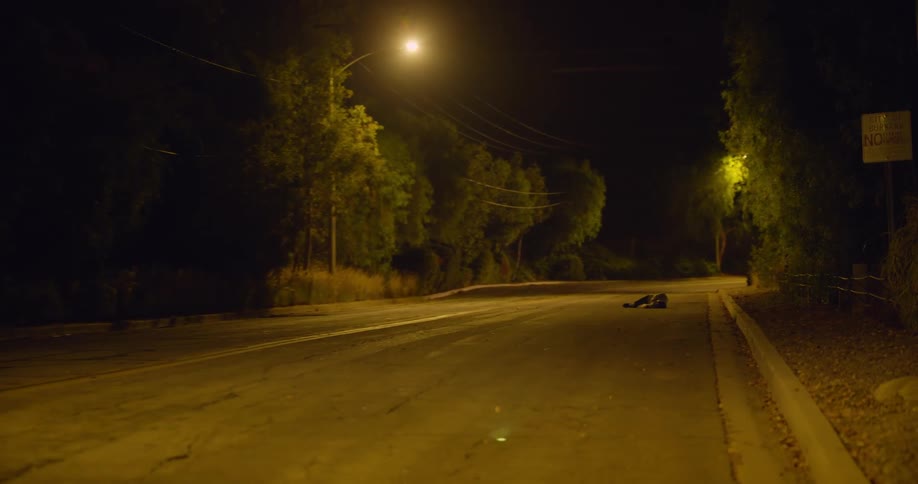 A man wearing a bloody shirt running down an empty road collapses in the street